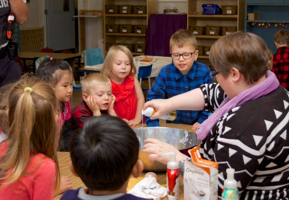 engaged children around a table as an ECE mixes items in a bowl 