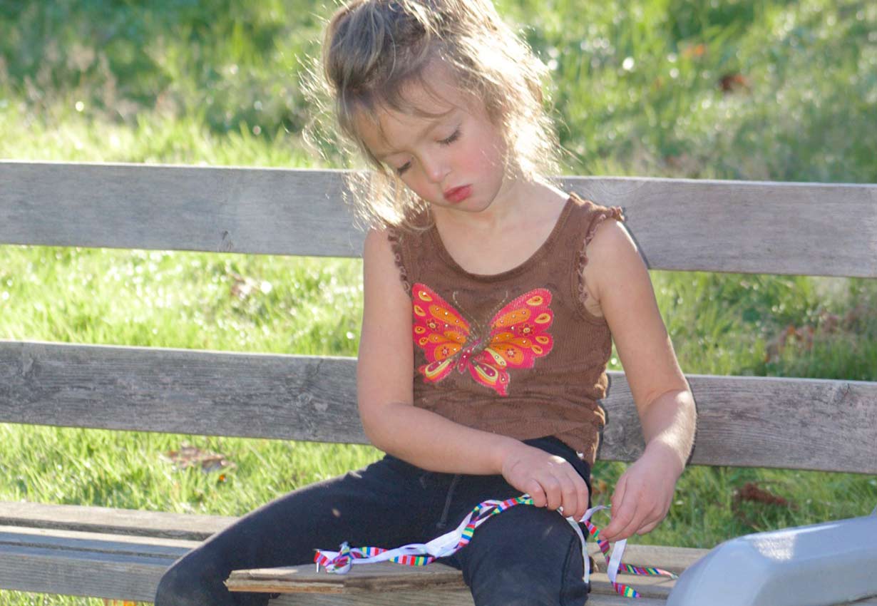 child sitting on a bench outdoors playing with ribbon