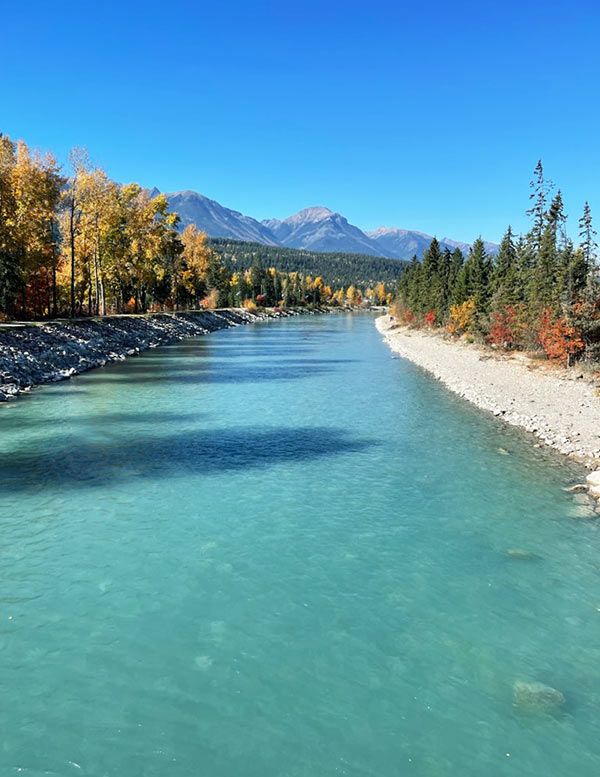 Photo 16: A picturesque fall landscape with trees lining a blue river and mountains as the backdrop