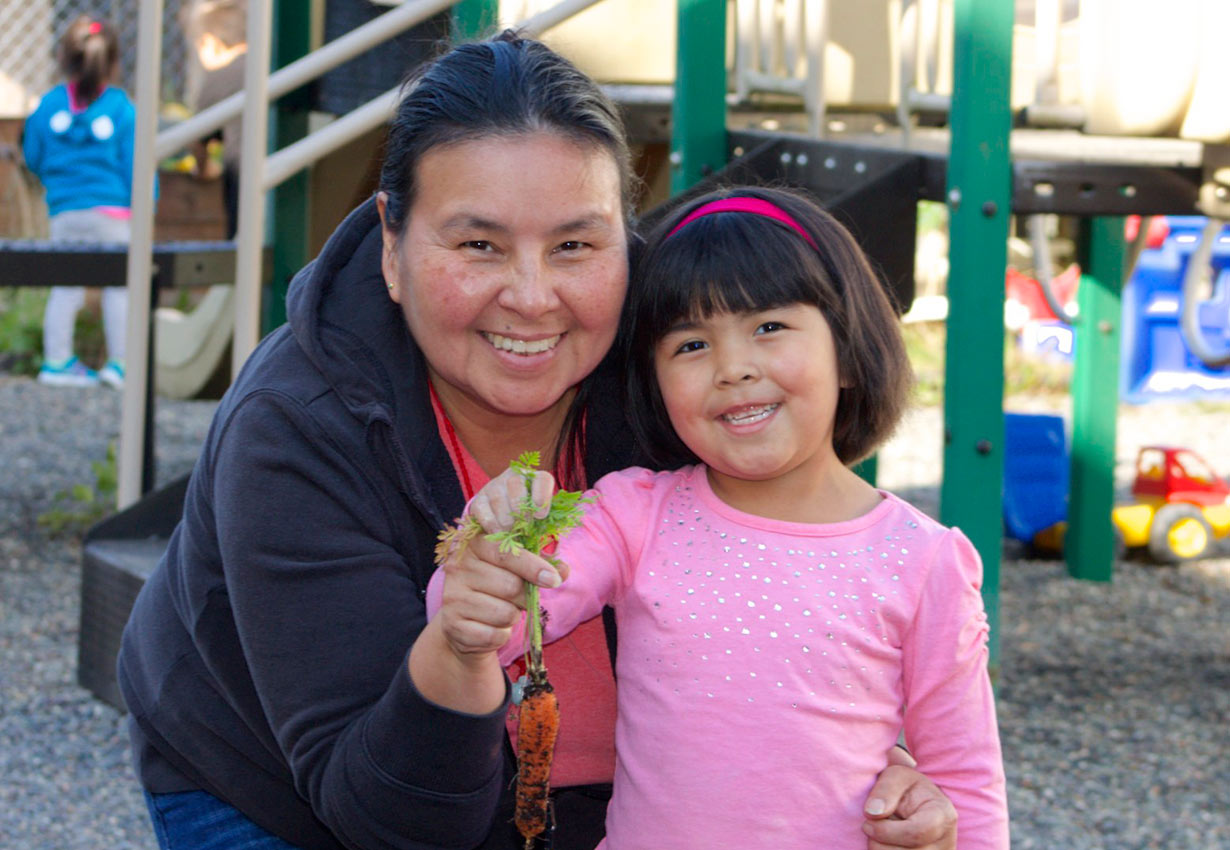 Early childhood educator and child holding up a carrot from a garden